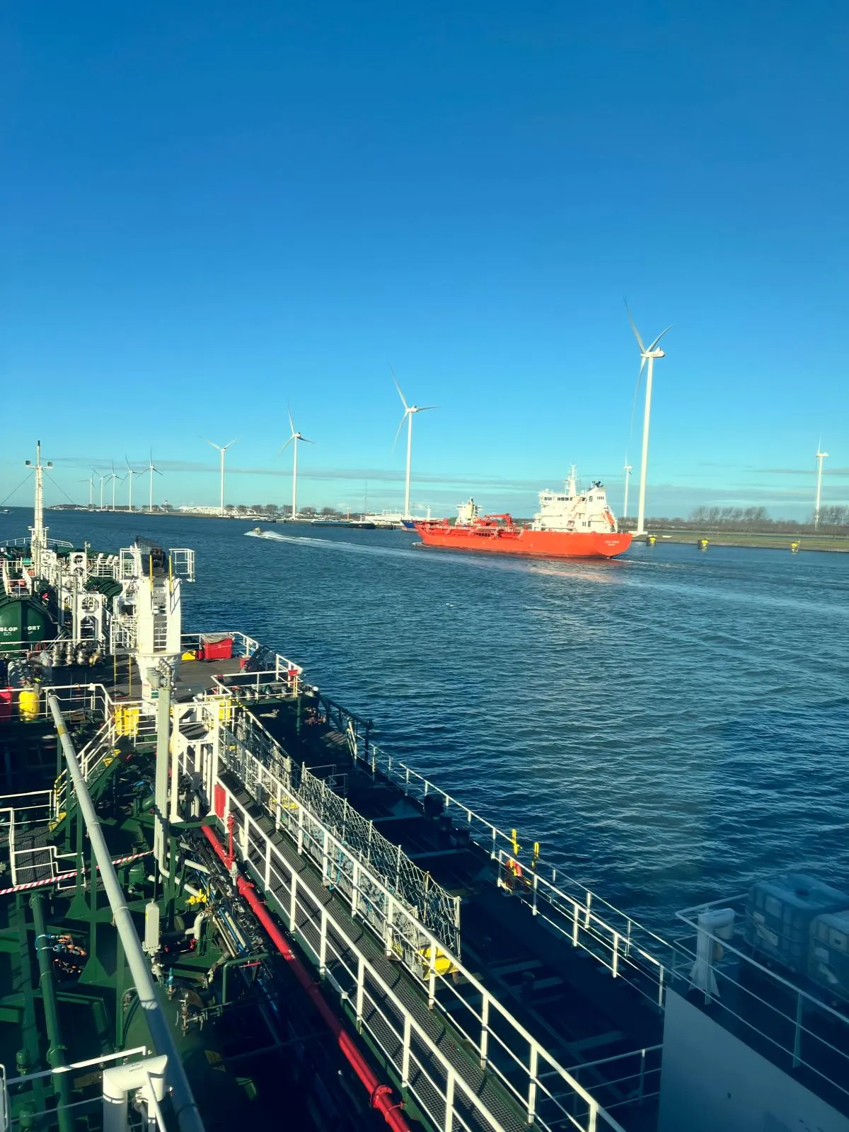 A tanker deck alongside a red vessel underway near an offshore wind farm