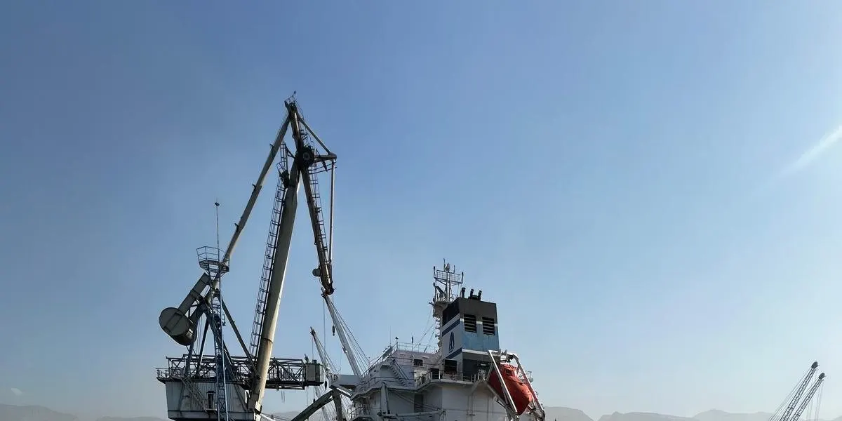 Vessel alongside with deck cranes raised against a clear sky