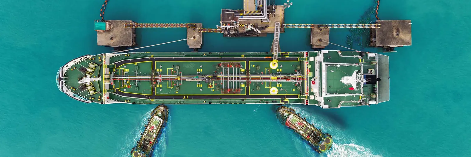 Large tanker vessel being guided to a jetty by tugboats